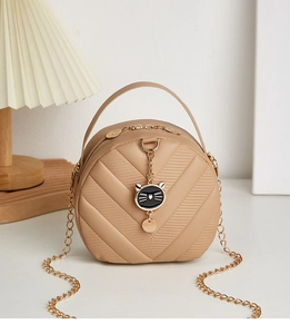 Detail of warm brown PU leather round crossbody bag with chevron texture and cat pendant