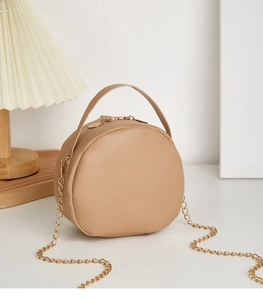 Detailed close-up of a round beige mini crossbody bag with gold chain and top handle