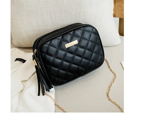 Detail of black quilted crossbody bag with golden chain strap and tassel on soft sofa