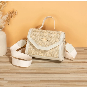 Close-up of beige woven straw bag featuring gold buckle and wide fabric shoulder strap