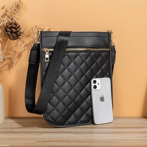 Sac bandoulière noir matelassé avec sangle large et boucles dorées sur table en bois