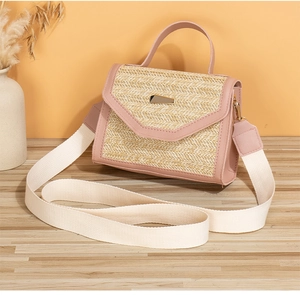 Close-up of straw crossbody bag with pink leather trim and golden metal buckle details