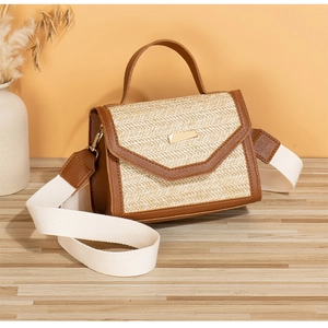Detail of summer straw bag featuring brown leather trim and golden metal clasp on wood surface