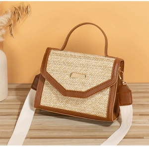 Detail of straw woven crossbody bag with brown leather trim and golden clasp on wood