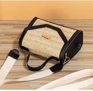 Detail of trendy straw crossbody bag featuring black trim and golden trapezoid lock