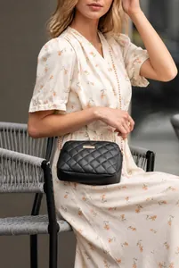 Detail van een zwarte gewatteerde crossbodytas met gouden ketting gedragen door model