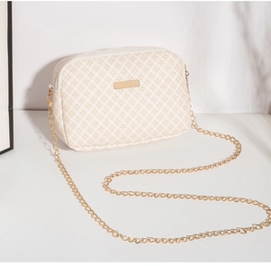 Detail van beige gewatteerde mini crossbody tas met gouden ketting en metalen plaatje
