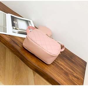Pink quilted crossbody camera bag with detachable coin purse on a wooden surface