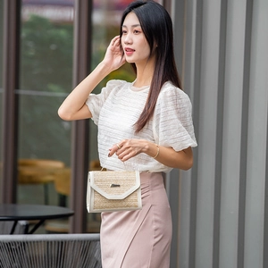 Women's chic beige straw handbag with white leather trim and metal clasp on outdoor model