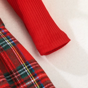 Detail of red ribbed knit sleeve and festive plaid tartan skirt on a plush background