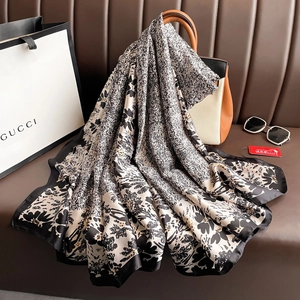 Elegant black and white floral satin silk scarf draped over a brown designer handbag