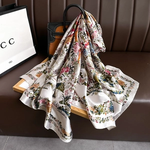Satin floral silk scarf with colorful botanical and bird prints draped on a leather bag