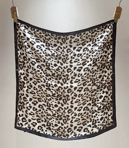 Detail of leopard print silk scarf with black border hanging on wooden clips
