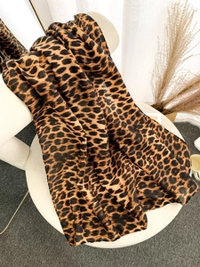 Detail of leopard print scarf with soft drape texture on minimalist white stool