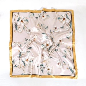 Close-up of white magnolia floral print on beige satin square scarf with gold border