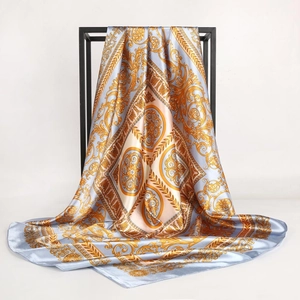 Detail showing the glossy golden Baroque pattern on a light blue satin silk square scarf