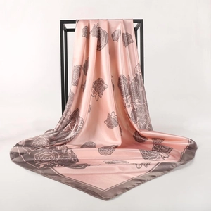 Pink silk scarf with grey rose print and contrasting borders hanging on a frame