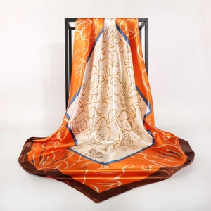 Detail of satin square scarf featuring golden floral lines and elegant orange color blocking