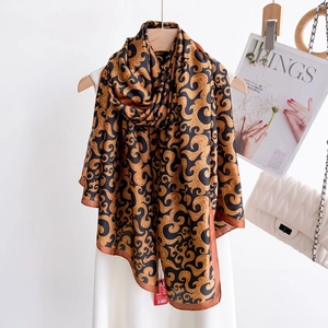 Retro black and gold silk scarf with vintage swirl patterns hung on a wooden hanger