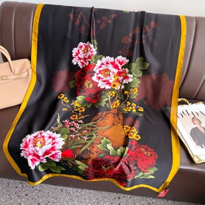 Macro detail of elegant black satin silk scarf with peony floral print on a leather sofa