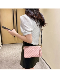 Sac bandoulière rose matelassé en V avec sangle logo tendance porté par un mannequin