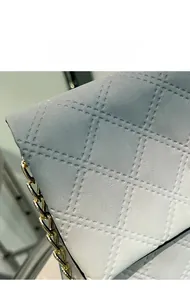 Macro detail of quilted rhombus pattern on light blue textured fabric with gold chain strap