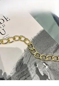 Macro detail of glossy light gold chain strap resting on a book for women's crossbody bag