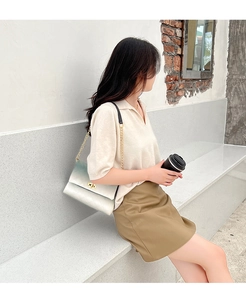 Outdoor lifestyle shot of a gradient white to green quilted shoulder bag with gold chain