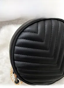 Detail of black quilted round bag featuring golden chain strap and V-shaped stitching