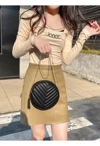 Detail of round quilted crossbody bag with gold chain strap and black tassel