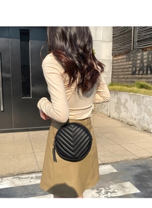 Close-up of black round quilted crossbody bag with gold chain strap and tassel