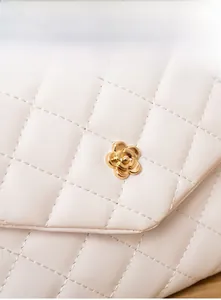 Close-up of white quilted leather texture and golden camellia flower metal buckle on bag