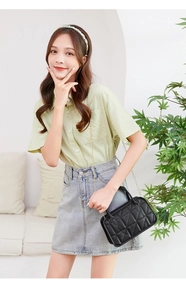Model wearing a black quilted crossbody bag with gold chain strap in a cozy interior