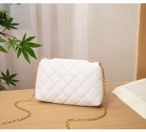 Détail d'un sac bandoulière blanc matelassé avec chaîne dorée sur table en bois