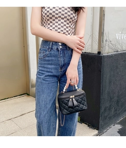 Détail du sac seau noir matelassé avec poignée perle et chaîne dorée en décor urbain chic