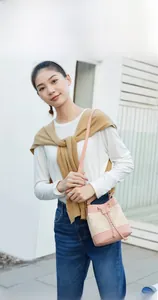 Outdoor model display of a pink and beige woven straw bucket bag with leather strap