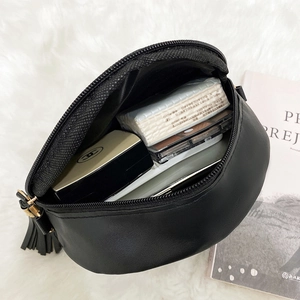 Minimalist black round crossbody bag with tassels and makeup items inside