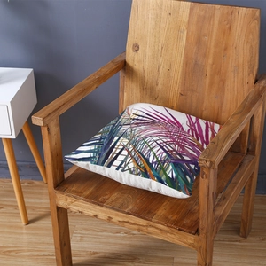 Tropical leaf print pillow cover on wooden chair with vibrant botanical patterns