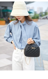 Close-up of black quilted small square bag with gold chain strap on a blue blouse model