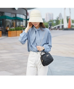 Detail of quilted black leather chain bag styled with a blue bow-tie blouse
