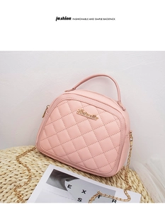 Pink quilted crossbody bag with gold chain strap and logo plate on a rustic mat