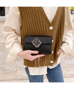 Detail der schwarzen Stepptasche mit goldener Kette und geometrischem Schnallenverschluss