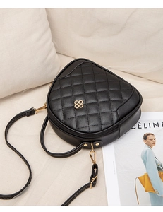 Detail of black quilted heart-shaped leather bag with golden clover logo and metal zipper