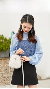 Sac bandoulière blanc matelassé avec emblème de trèfle doré porté par le modèle
