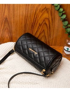 Makroaufnahme der schwarzen gesteppten Zylindertasche mit Golddetails auf weißem Strickstoff