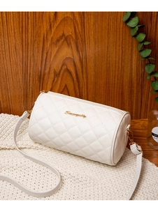 Detail einer weißen gesteppten Zylindertasche mit goldenem Logo auf Holzuntergrund