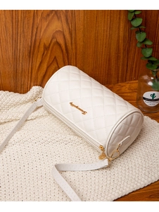 Detailaufnahme der weißen gesteppten Zylindertasche mit goldenem Logo auf einem Strickteppich