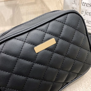 Detail shot of black quilted faux leather crossbody bag with gold metal rectangle plate