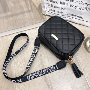 Detail of black quilted crossbody bag featuring gold hardware and a printed woven strap