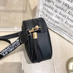 Detail of black quilted bag with gold hardware, leather tassel, and patterned strap